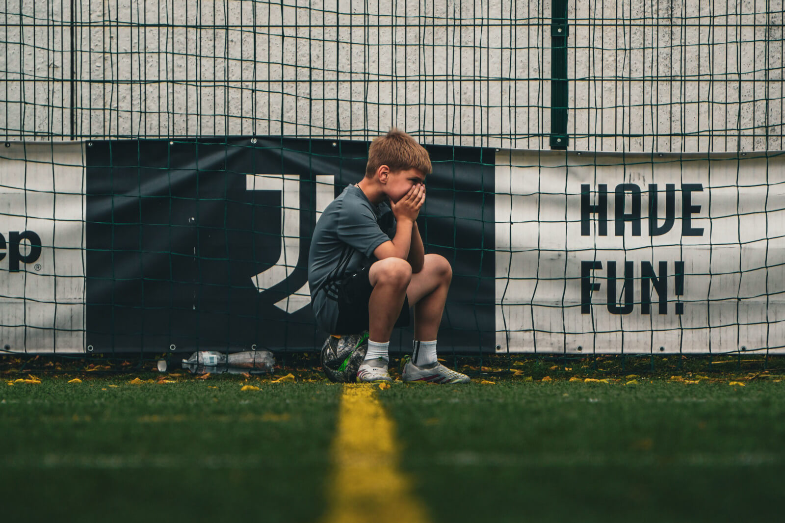 youth-sports-dropout young soccer player alone on field sitting on soccer ball